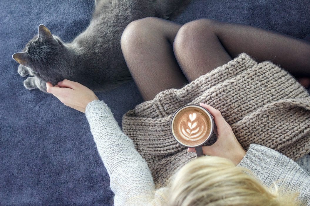 Woman petting a cat drinking a coffee for mindfulness.