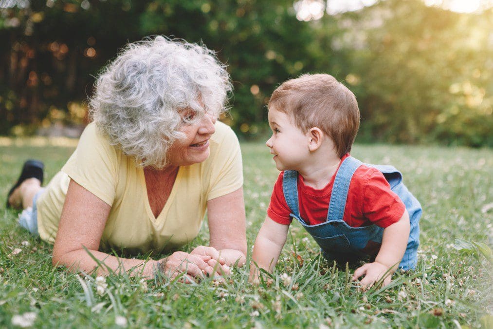 Grandson lying down with his grandma in the grass.